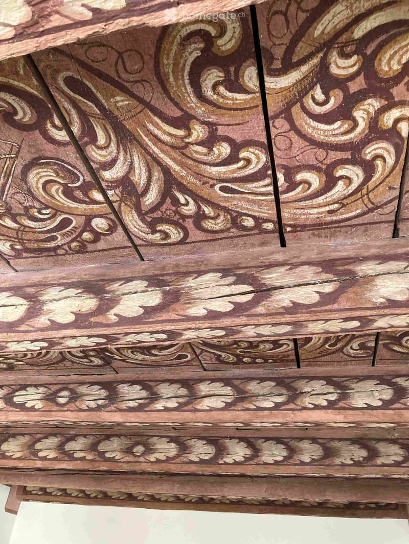 An intricately carved wooden ceiling with floral and scrollwork patterns in warm brown and gold tones.