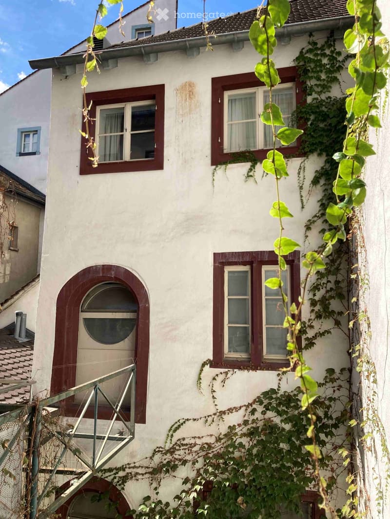 Two-story white house with red-framed windows, ivy-covered walls, and a small balcony with metal railing.