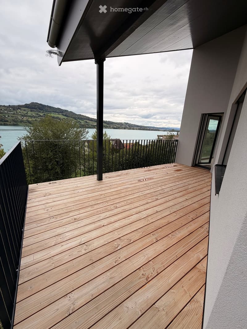 Wooden deck with black metal railing, overlooking a lake and hills.