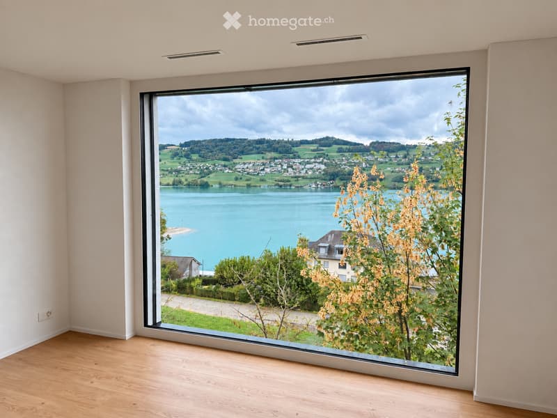 Empty room with large window showcasing a scenic view of a lake and surrounding landscape.