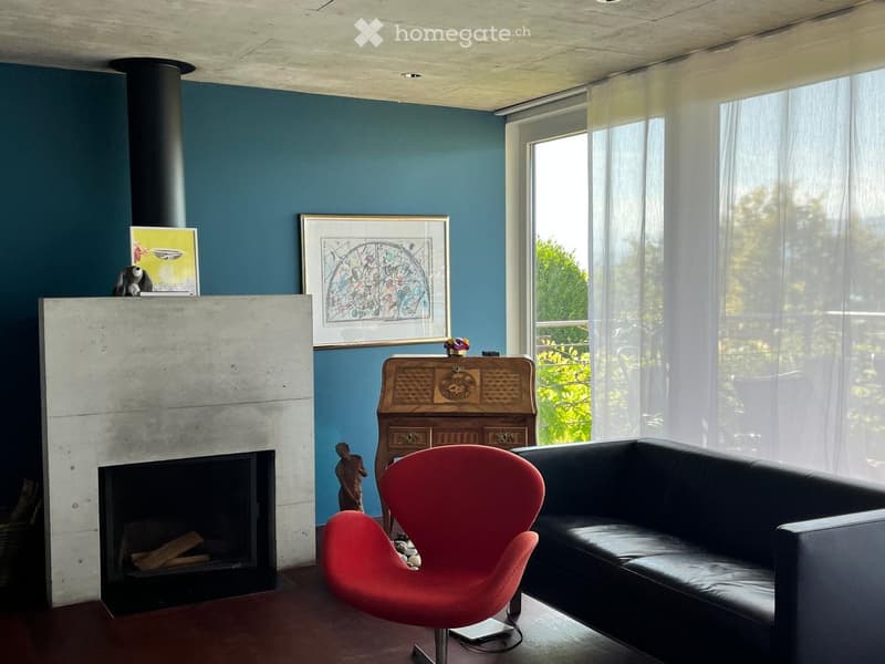 Living room with a fireplace, a red chair, a black sofa, a wooden table, and framed artwork on the wall.