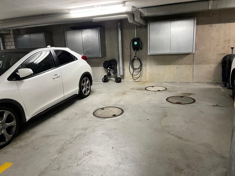 Underground parking area with a white car, a baby stroller, and an electric vehicle charging station.