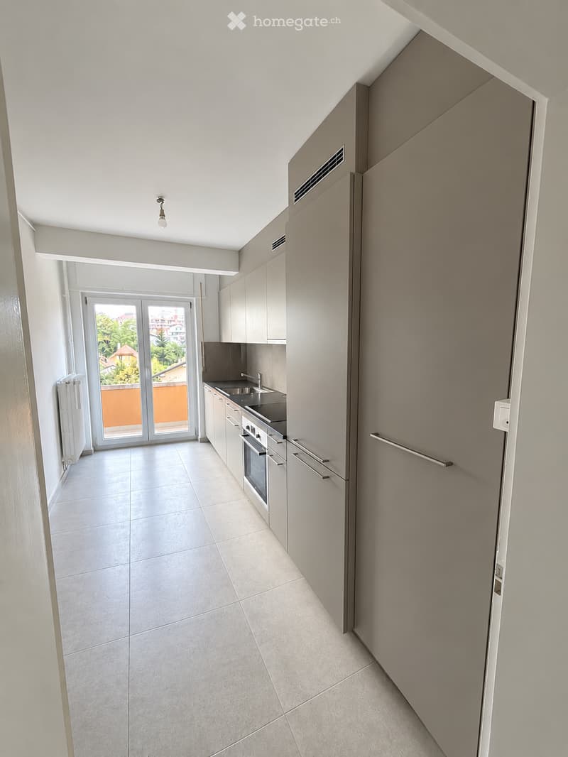Modern kitchen with white cabinets, stainless steel sink, oven, and a sliding glass door leading to a balcony.