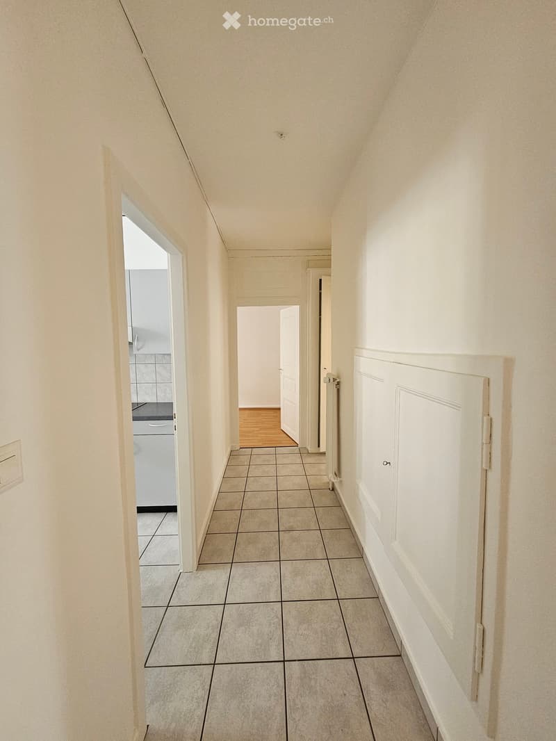 Empty hallway with tiled floor, white walls, and several doors leading to other rooms.