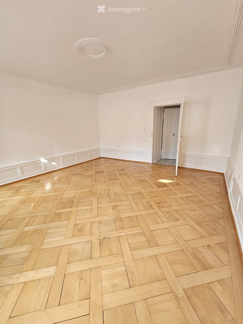 Empty room with light wooden herringbone flooring, white walls, and a white ceiling with a decorative light fixture.
