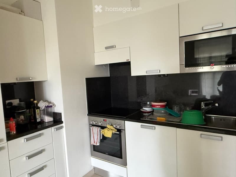 Modern kitchen with white cabinets, stainless steel appliances, black countertops, and various kitchen items on the counter.