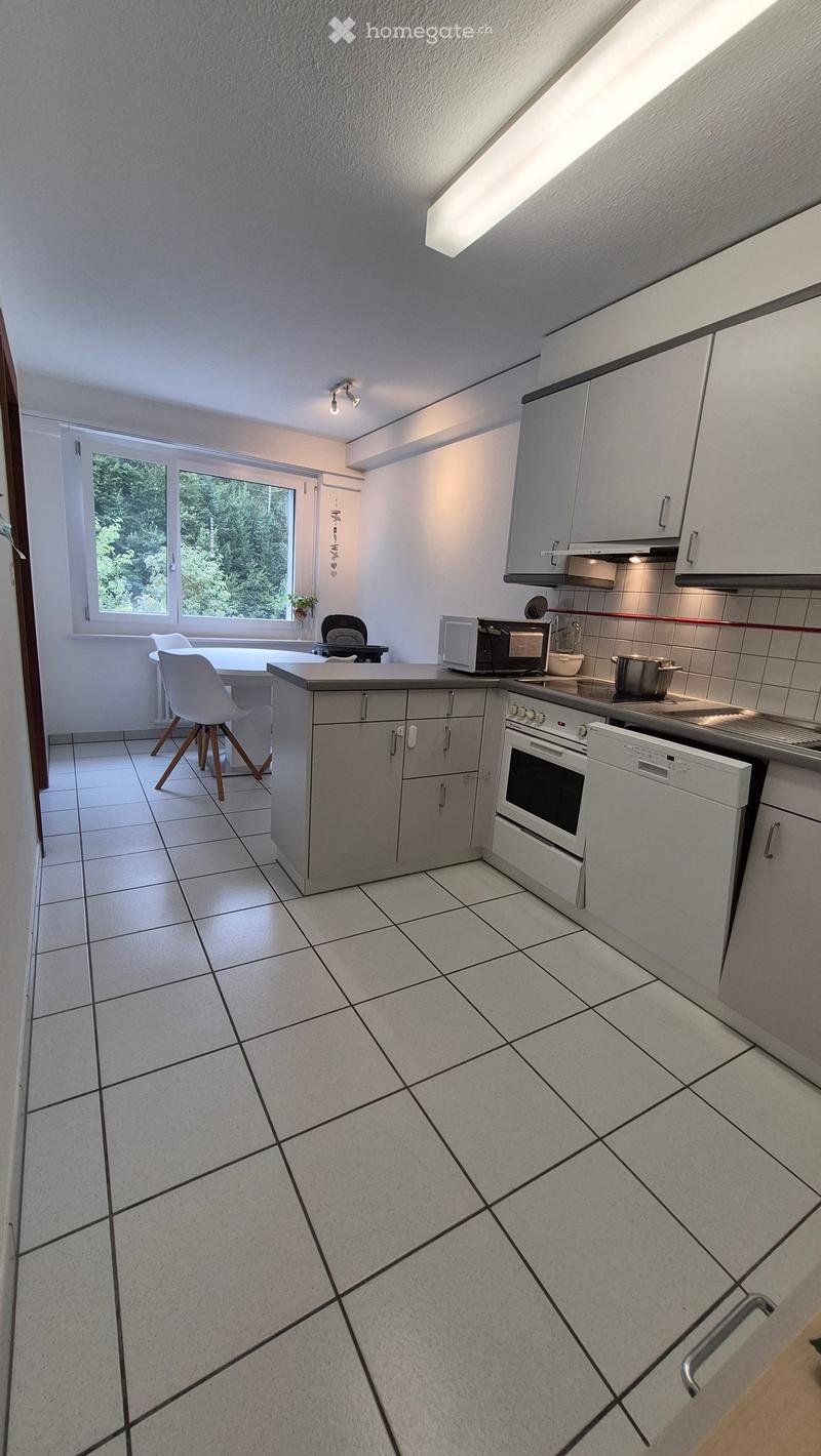 Modern kitchen with white cabinets, stainless steel appliances, tiled floor, and a large window overlooking greenery.