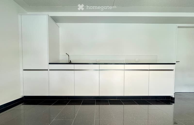 Empty kitchen with white cabinets, black countertops, stainless steel faucet, and built-in electrical outlets.