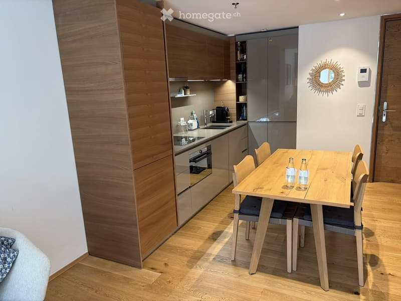Modern kitchen and dining area with wooden cabinets, a sink, an oven, a dining table with chairs, and a decorative mirror on the wall.