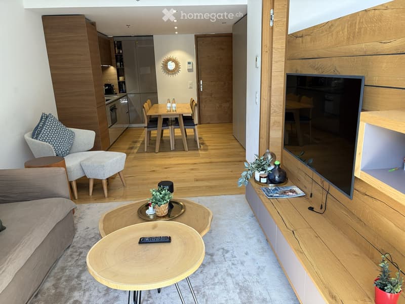 Modern living and dining area with a sofa, coffee table, ottoman, dining table, chairs, and a kitchen area with appliances.