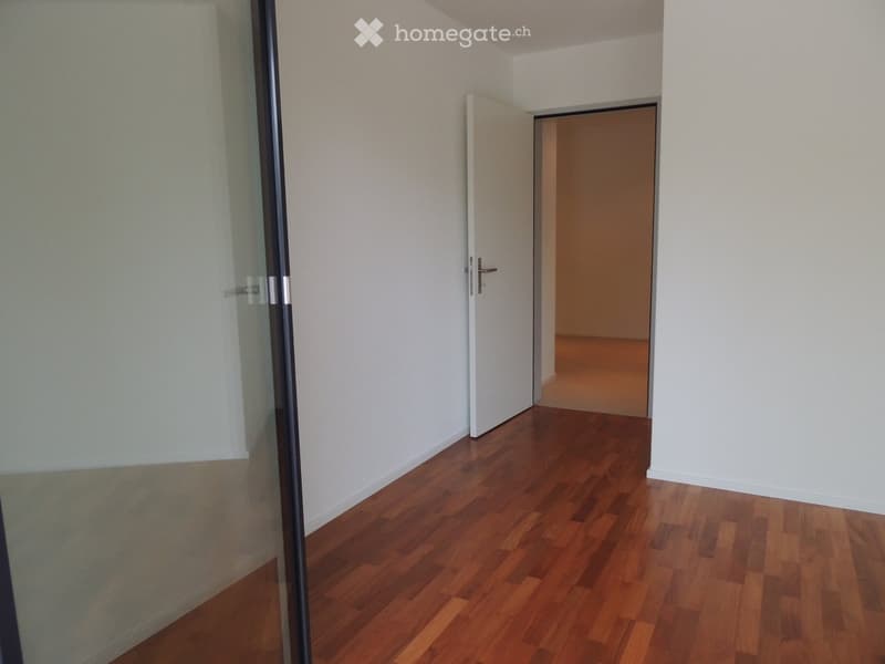 Empty hallway with wooden flooring, white walls, and two open doors leading to other rooms.