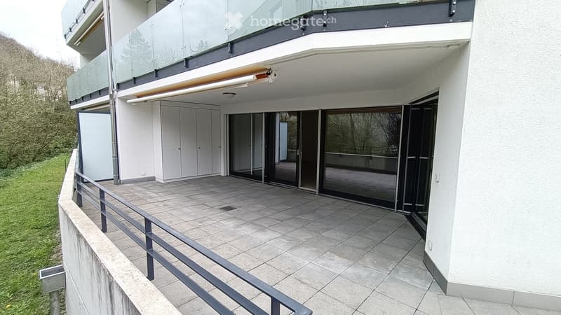 Modern balcony with tiled flooring, glass railings, and a view of the surrounding greenery.