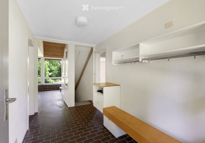 Entrance hall with brown floor tiles, white walls, a bench, a wooden ceiling, and a small built-in wardrobe.