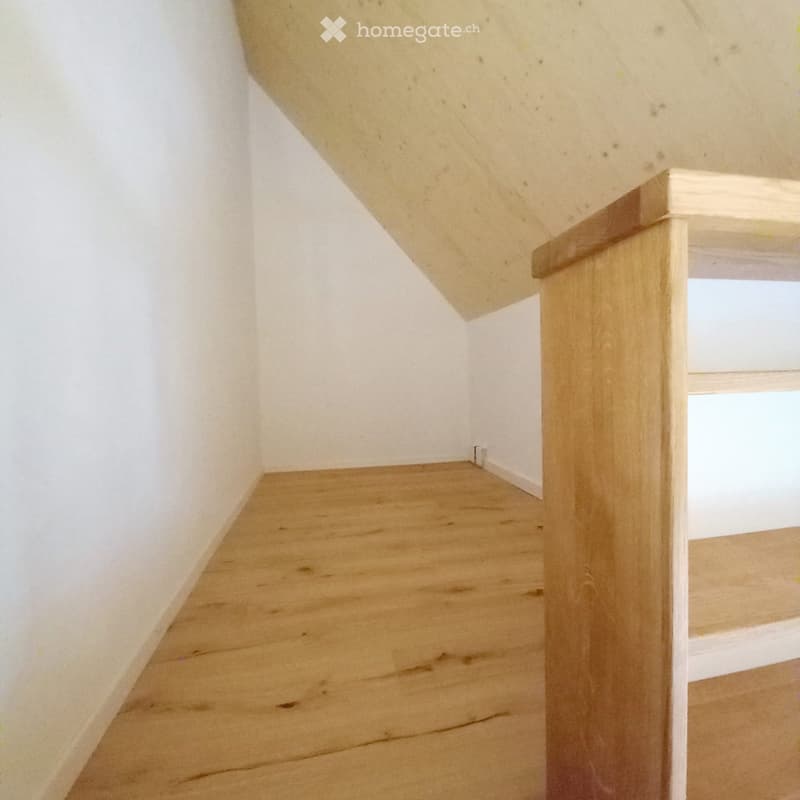 Empty wooden staircase with white walls and a slanted ceiling, leading to a small windowed area.