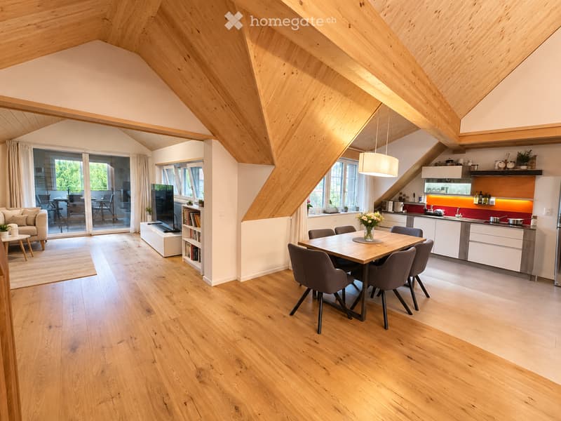 Open-plan living and dining area with wooden floors, exposed wooden beams, large windows, and a modern kitchen. Features include a sofa, coffee table, bookshelf, TV, dining table with chairs, and kitchen cabinets.