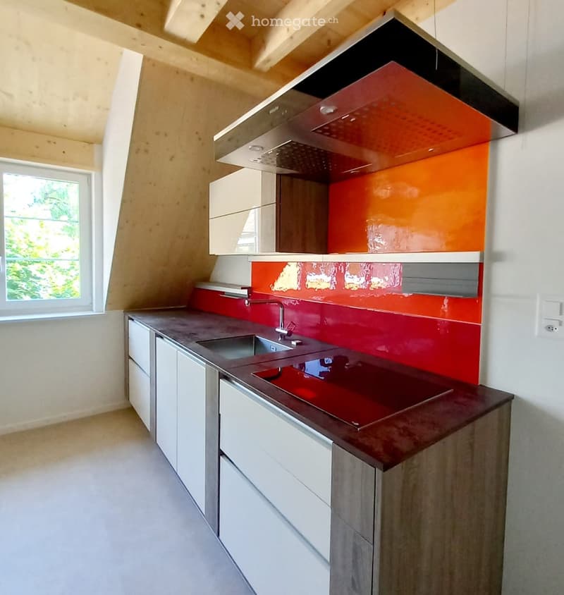 Modern kitchen with white cabinets, dark countertop, red backsplash, and stainless steel sink.