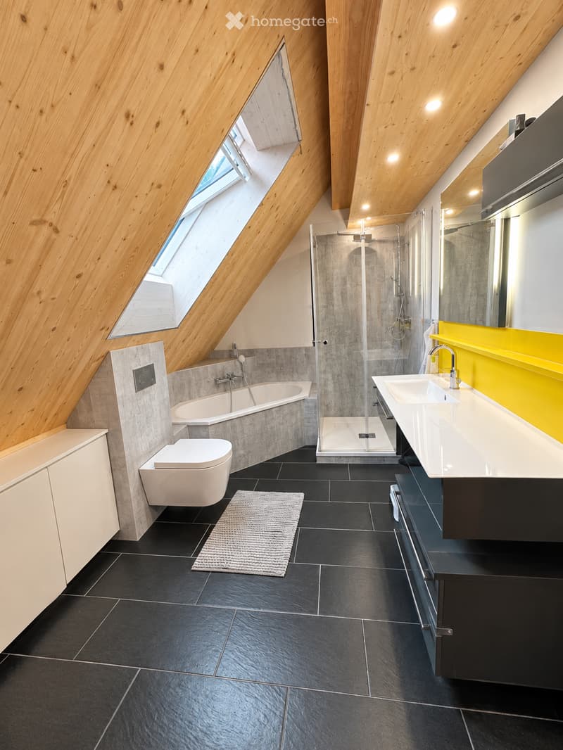 Modern bathroom with a sloped wooden ceiling, black tiled floor, white bathtub, toilet, double sink with yellow countertop, and a glass-enclosed shower area.