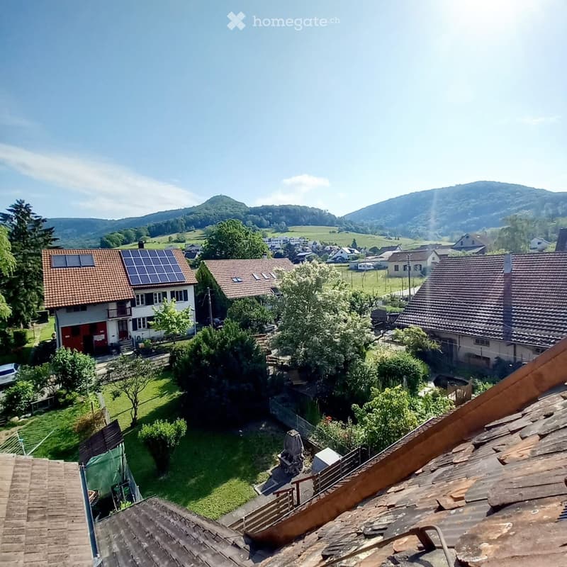 Aerial view of a residential area with houses, green lawns, trees, and a scenic mountainous backdrop.