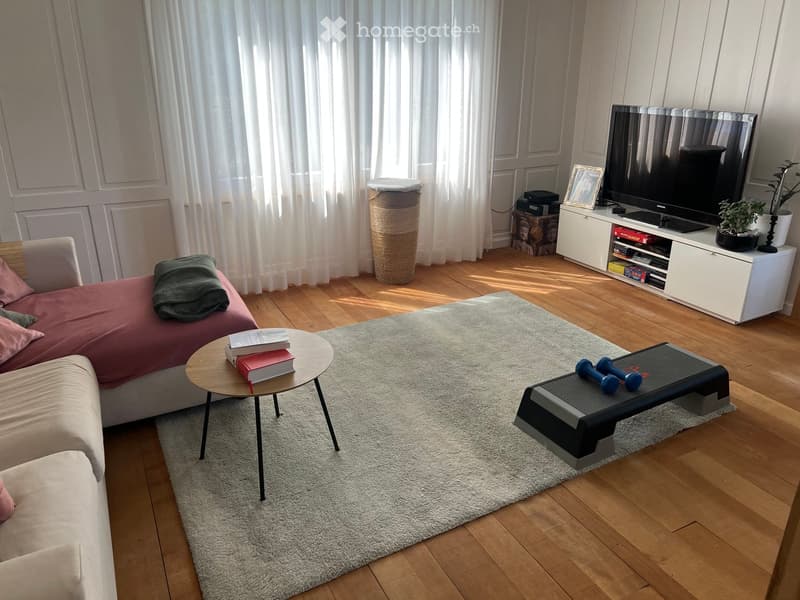 Modern living room with a light-colored sofa, coffee table, TV stand, and exercise equipment.