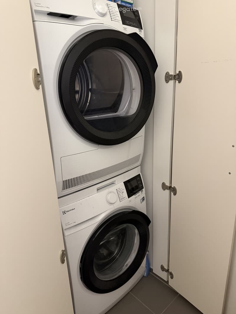 A compact bathroom with a stacked washing machine and dryer unit, white walls, and a tiled floor.