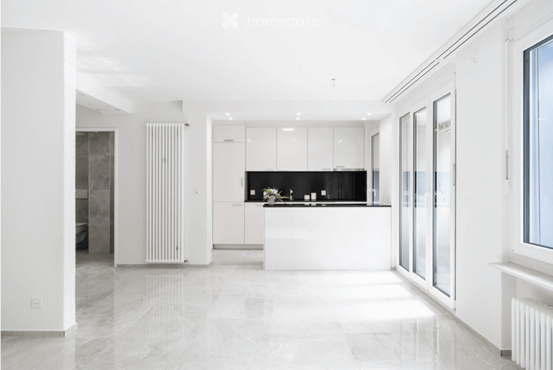 Modern, minimalist kitchen with white cabinets, a black countertop, and a sleek sink area. The space features large windows and a polished tile floor.