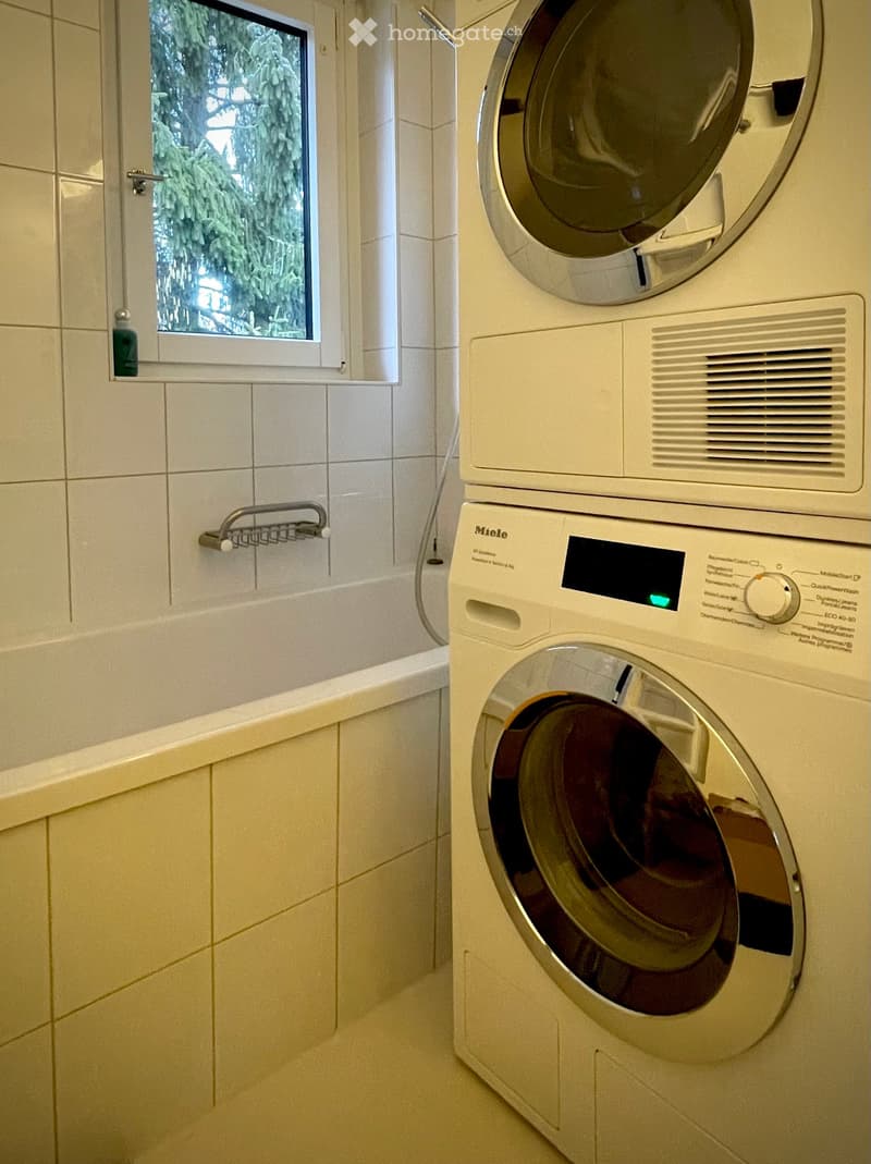Bathroom with a bathtub, a window, and a stacked washing machine and dryer unit.