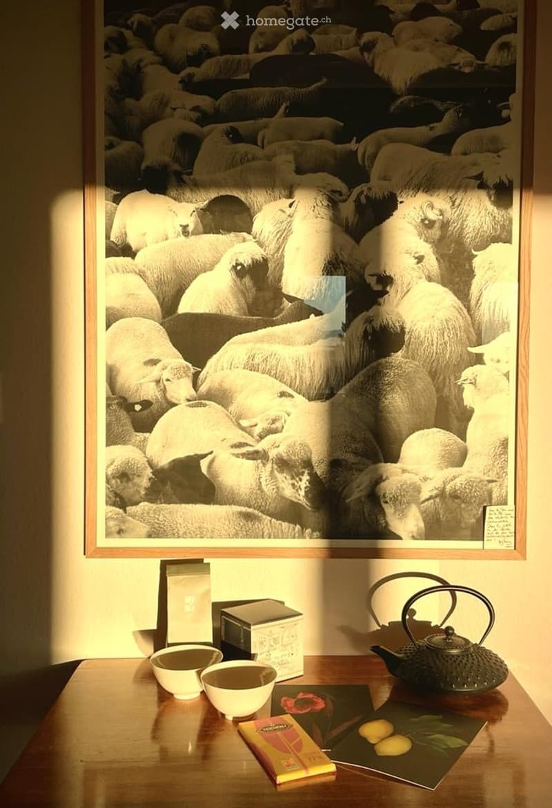 A wooden table with a teapot, bowls, and a framed black-and-white photograph of sheep on the wall behind it.