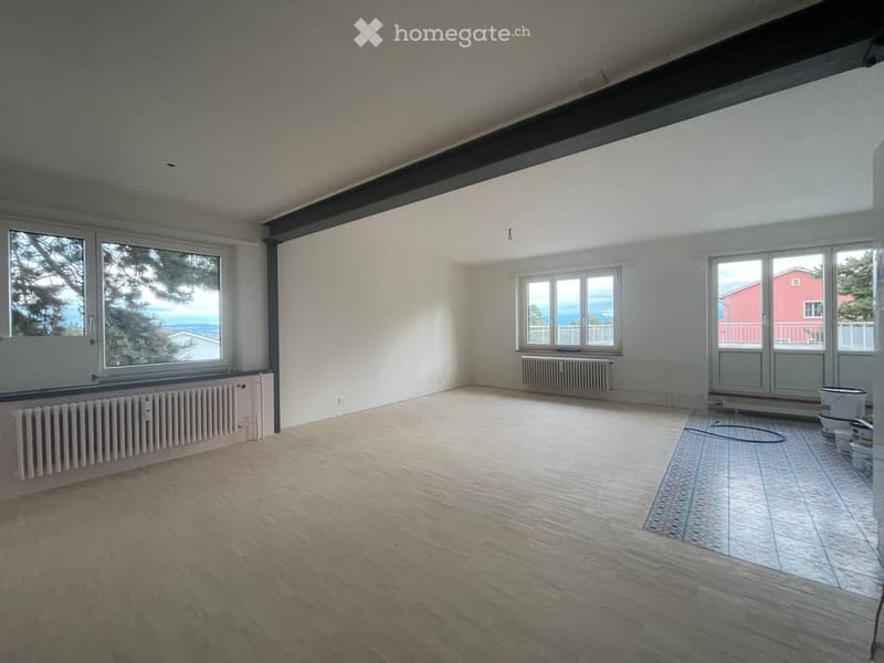 Empty room with wooden flooring, large windows, radiators, and a tiled area in the corner.