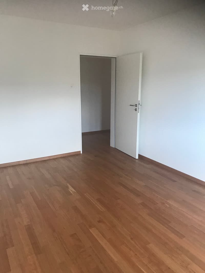 large room with wooden floors, white walls, white door and doorway leading to another room
