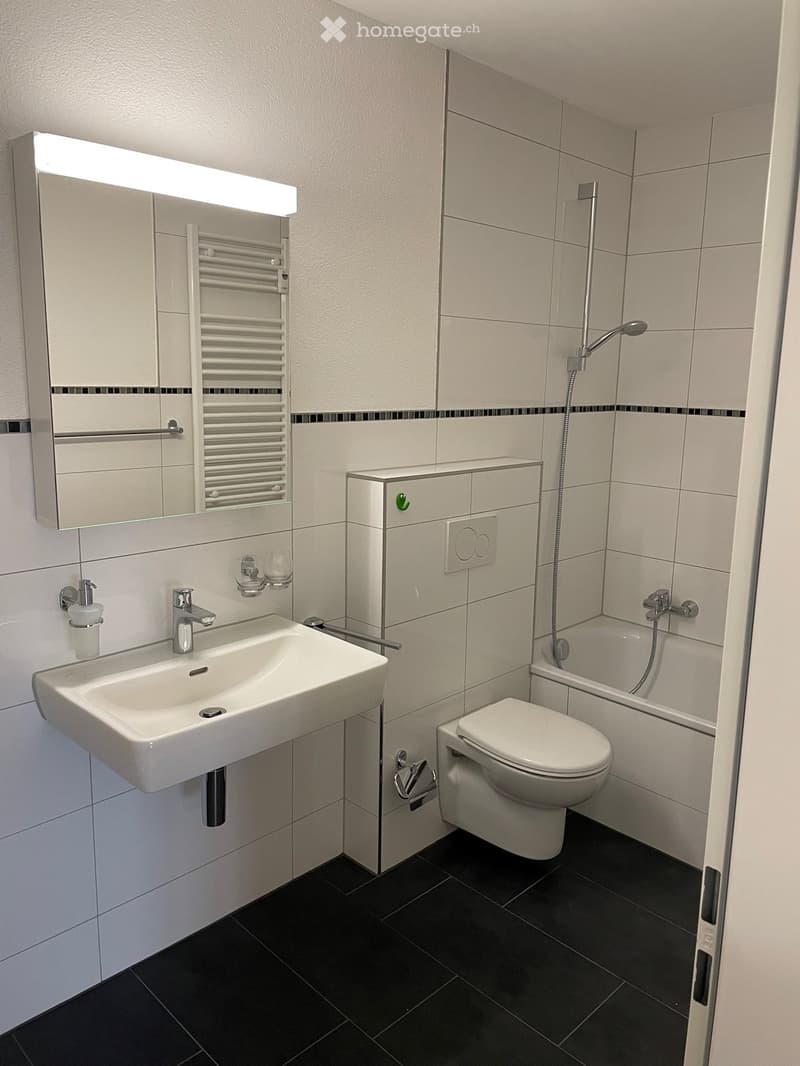 modern bathroom with white tiles, white sink, mirror with light, toilet, bathtub, shower, faucet