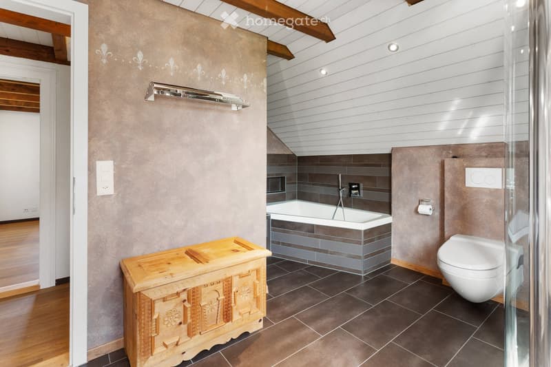 Bathroom with wooden floor, gray walls, wooden chest, bathtub, toilet, glass shower enclosure