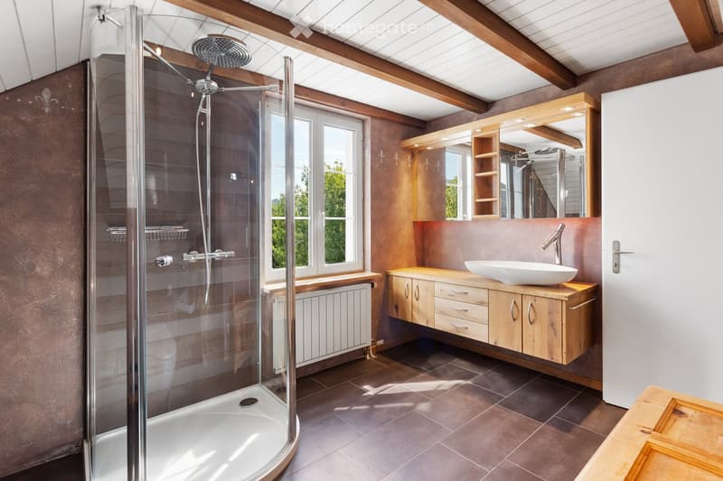 Bathroom with glass shower, wooden vanity, white sink, mirror, wooden shelves, radiator, tiled floor, wooden ceiling beams