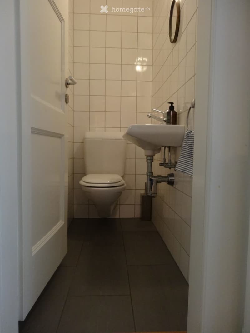 Small bathroom with white tiled walls, a toilet, a sink with a faucet, a soap dispenser, and a mirror above the sink.