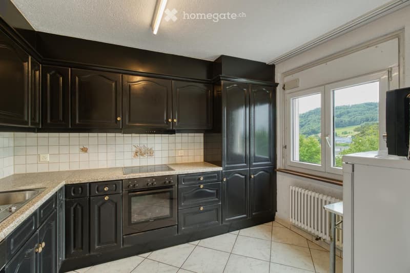 Modern kitchen with black cabinets, granite countertop, stainless steel oven, and large windows offering a scenic view.