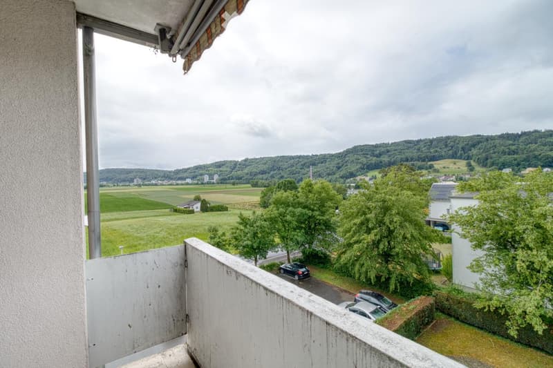 Balcony overlooking a rural landscape with fields, trees, and a small town in the distance.