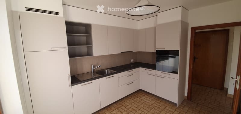 Modern kitchen with white cabinets, black countertop, stainless steel sink, and built-in oven.