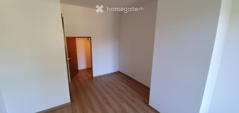 Empty room with white walls and wooden flooring, featuring a doorway leading to another room.