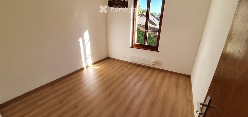 Empty room with wooden flooring, white walls, and a large window with wooden frame. No furniture or equipment present.