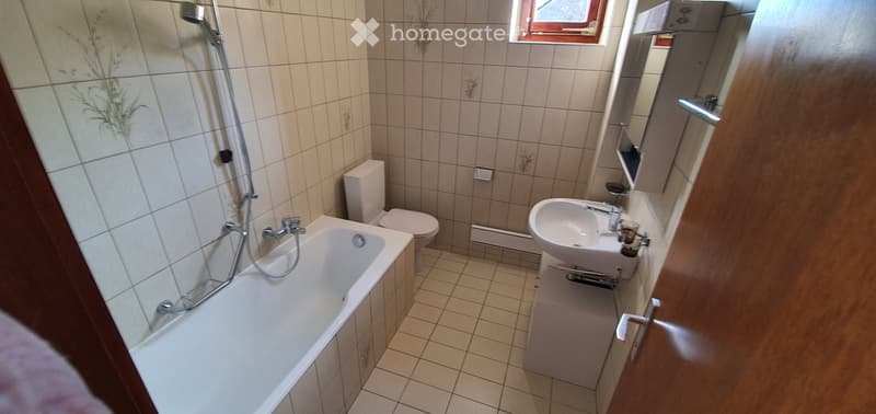 Bathroom with a bathtub, toilet, sink, mirror, and tiled walls.
