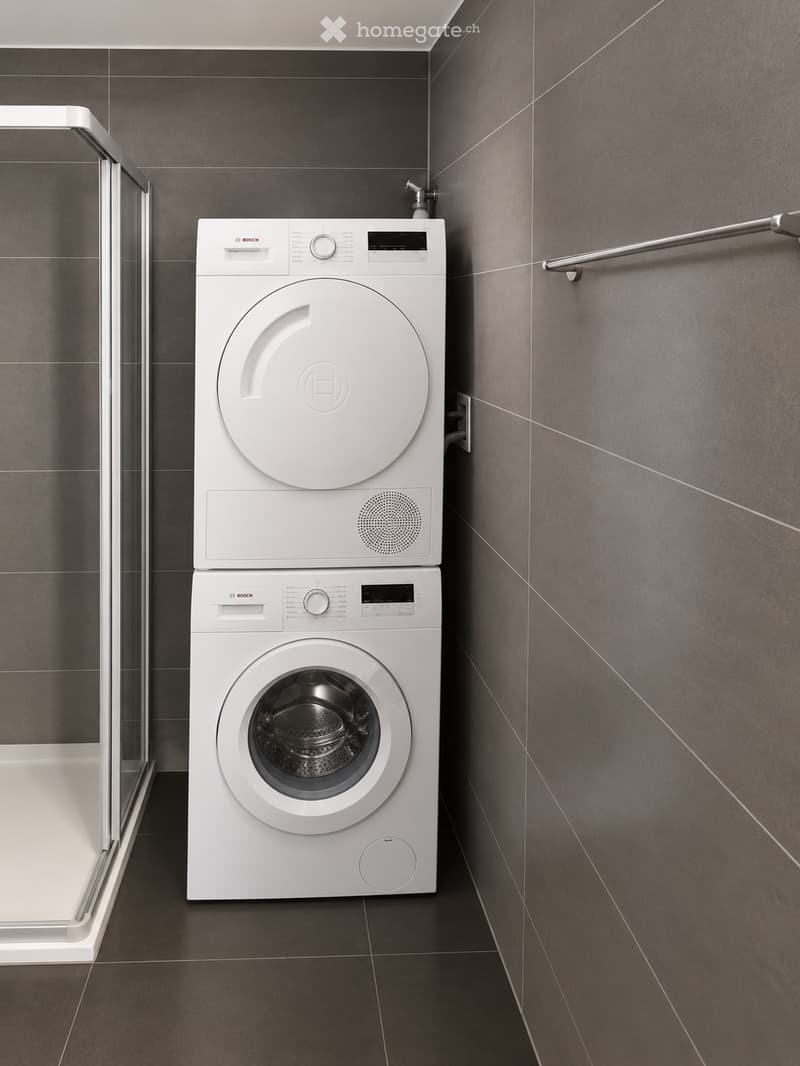 Modern bathroom with dark grey tiled walls and floor, featuring a stacked Bosch washing machine and dryer unit.