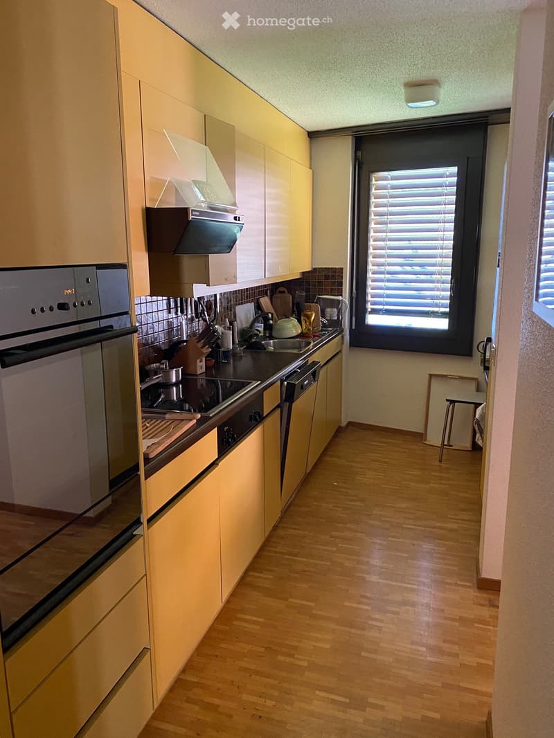 Compact kitchen with light wooden cabinets, a sink, microwave, and oven. The space is organized with various kitchen items and appliances.