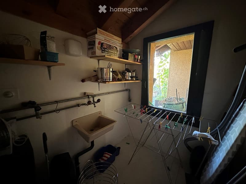 Utility room with a sink, shelves holding pots and boxes, a clothes drying rack, and a chair near the window.