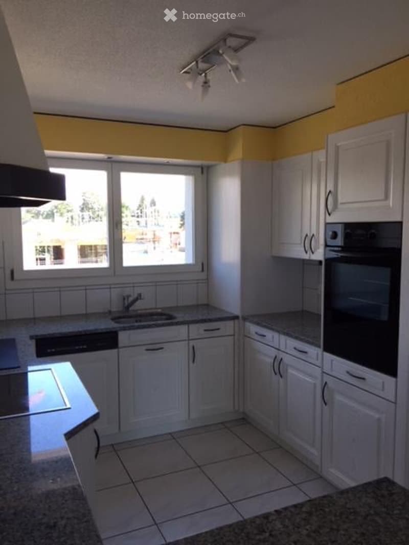 Bright kitchen with white cabinets, granite countertops, and a large window offering a view. Includes a sink, faucet, oven, and dishwasher.