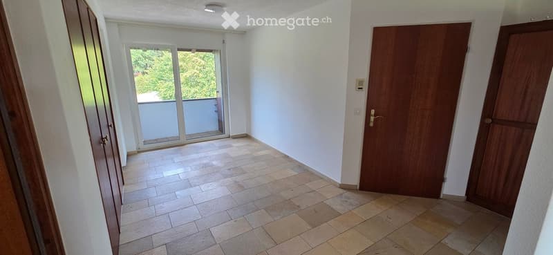 Empty hallway with tiled floor, white walls, and wooden doors leading to rooms and a balcony.