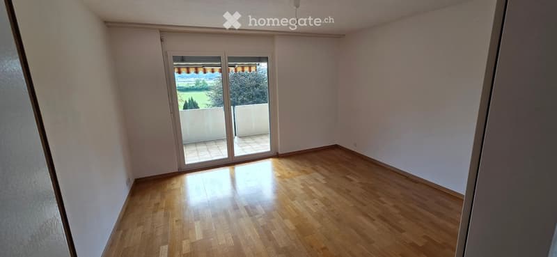 Empty room with wooden flooring, white walls, and large sliding glass doors leading to a balcony.
