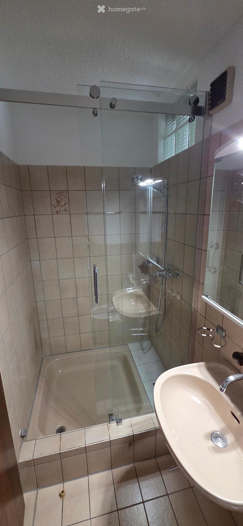 Modern bathroom with a bathtub, glass shower enclosure, and a sink. The walls are tiled in beige, and the floor is also tiled.
