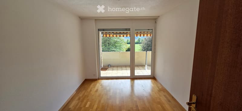 Empty room with wooden flooring, white walls, and large sliding glass doors leading to a balcony area.