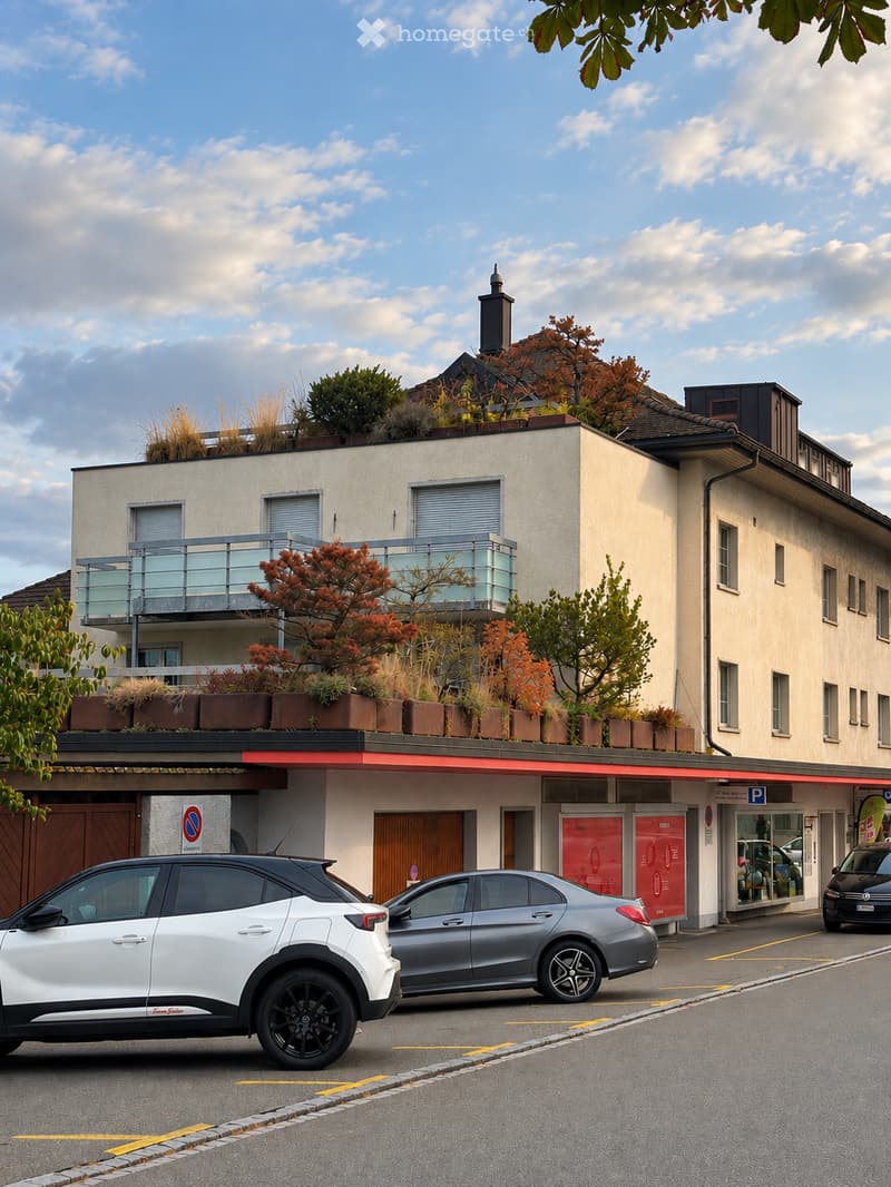 Modern multi-story building with a balcony, rooftop garden, and several parked cars in front.
