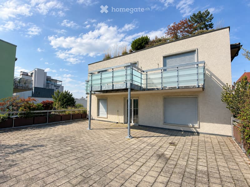 Modern two-story house with a balcony, garage, and surrounding greenery.