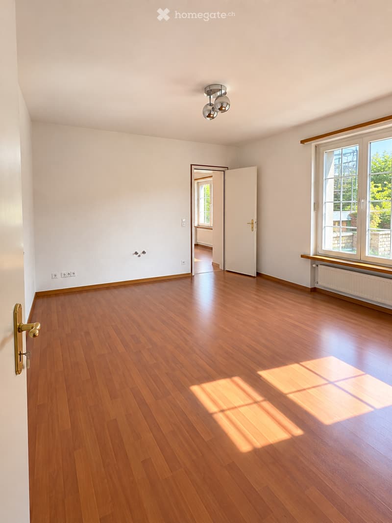 Empty room with wooden flooring, white walls, and large windows allowing natural light. No furniture or equipment is present.